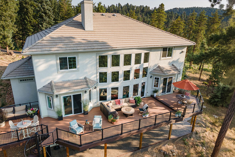 Evergreen, Colorado Trex deck featuring glass railings, steel framing, custom spiral stairs, LED lighting - drone shot.
